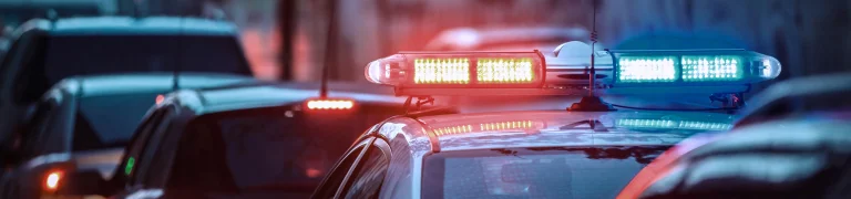 Police lights flashing atop a car, illuminating a city street at night.