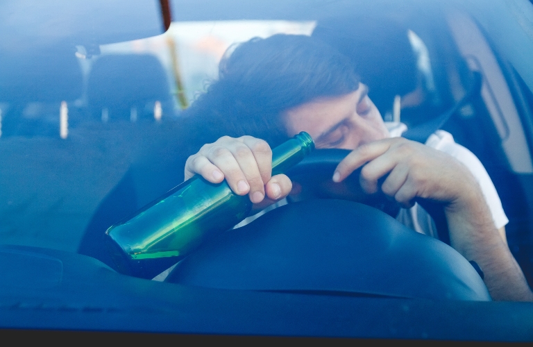 Drunk young man driving a car with a bottle of beer