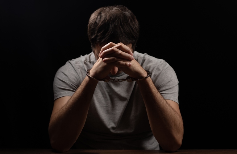 Handcuffed man covering his face with his hands