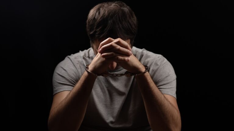 Handcuffed man covering his face with his hands