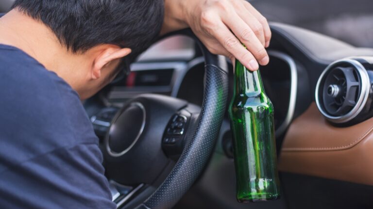 man is sleeping in the parked car and holding bottle of beer