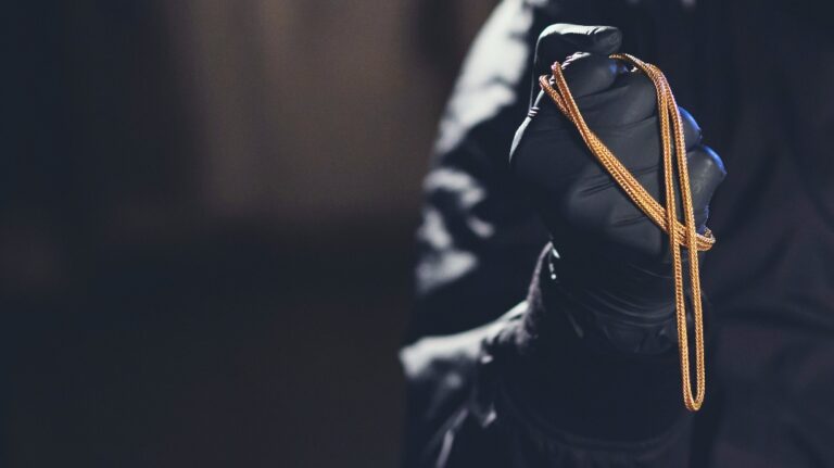 The robber is holding a gold chain in his hands