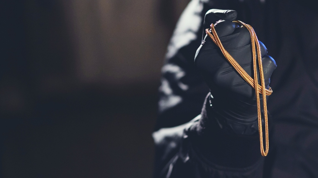 The robber is holding a gold chain in his hands