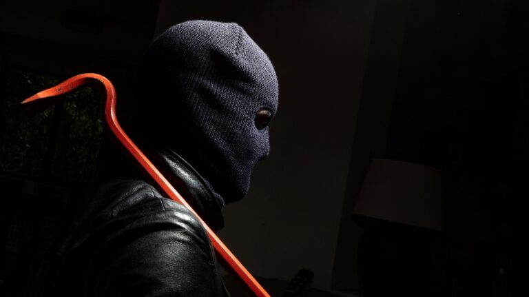Masked burglar in balaclava with red crowbar