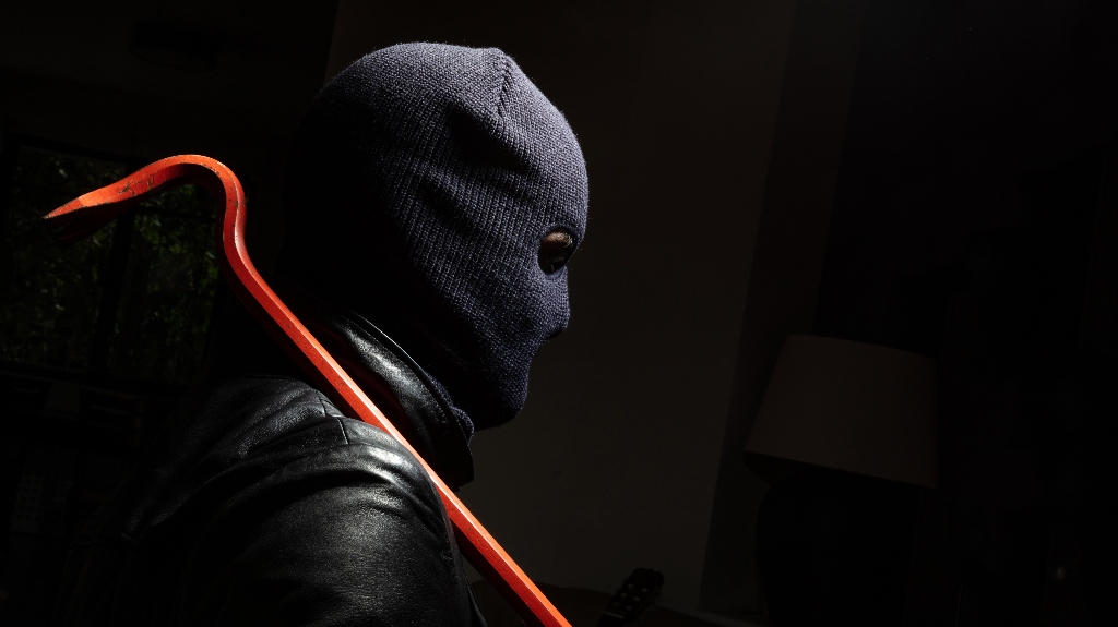 Masked burglar in balaclava with red crowbar
