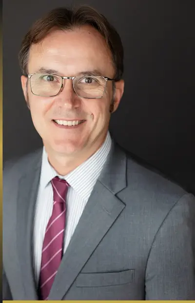 Professional headshot of a man wearing glasses, a gray suit, and a striped tie.