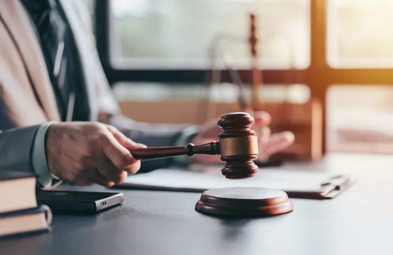 Person in suit holding wooden judge gavel above sound block on desk.