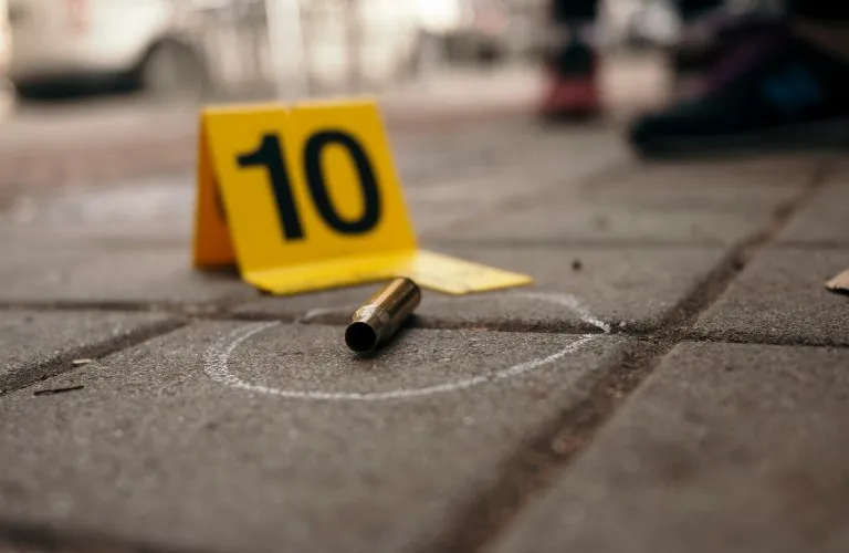 Close-up of a brass bullet casing on pavement, marked with a white chalk circle and yellow evidence marker numbered 10.