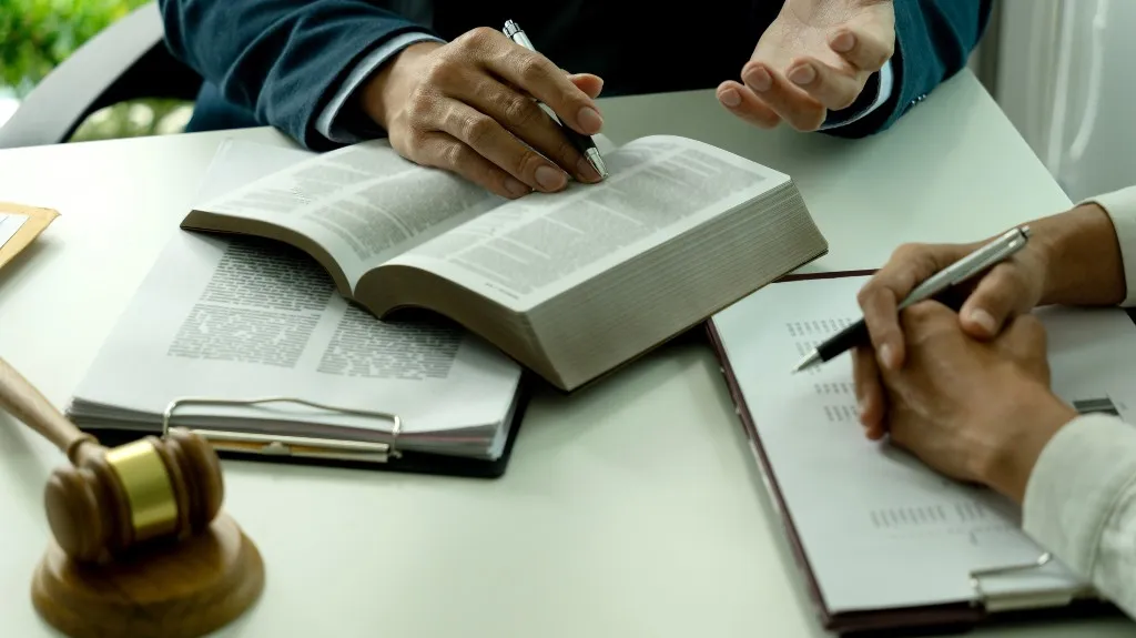 Two individuals reviewing legal documents with an open book, clipboard, and wooden gavel on a white table.