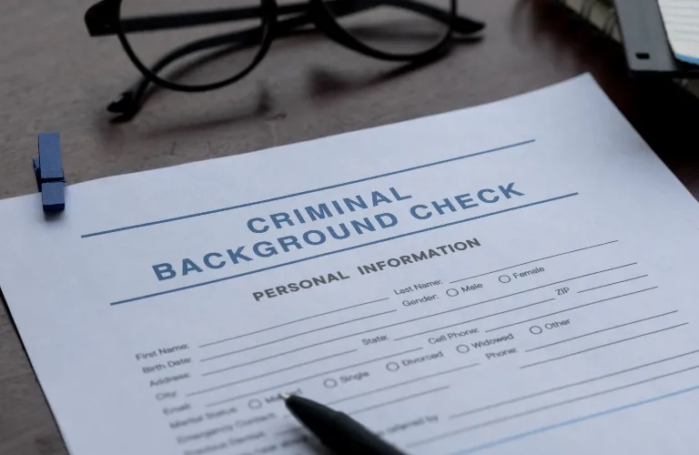 Criminal background check form on desk with black pen and eyeglasses nearby.