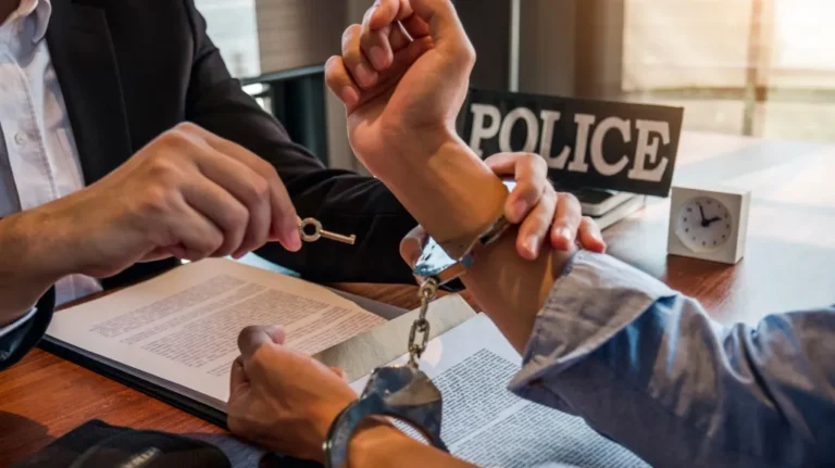 Person in handcuffs being unlocked with a key by an individual in formal attire at a desk.