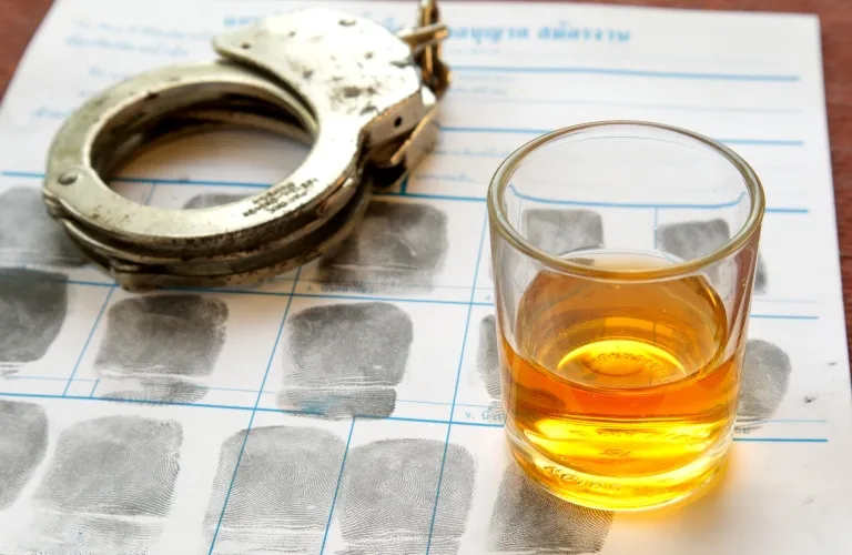 Metal handcuffs and a glass of amber liquid placed on a fingerprint identification sheet.