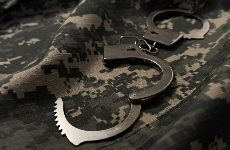 Metal handcuffs placed on digital camouflage military fabric in low light.