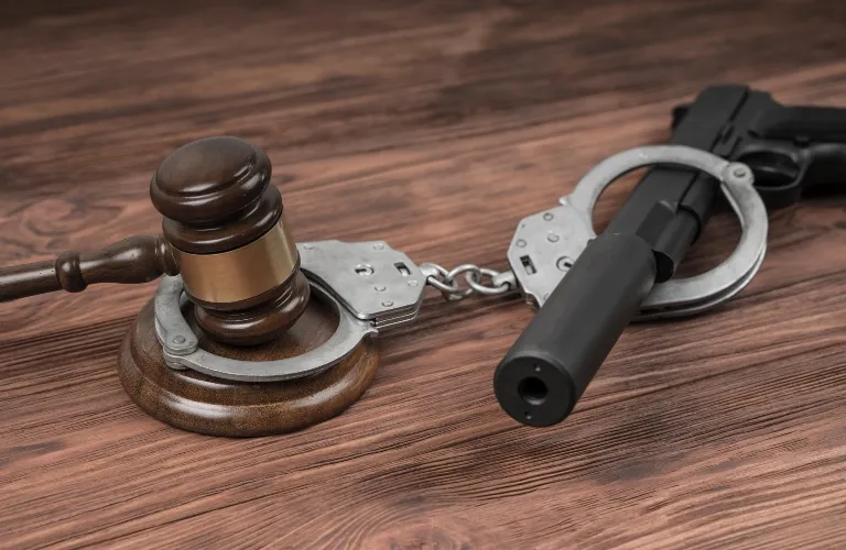 Wooden judge's gavel, metal handcuffs, and black handgun on wooden surface.