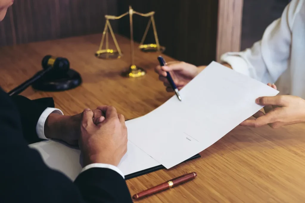 Two individuals at a wooden desk reviewing a document, with a gavel and scales of justice in the background.