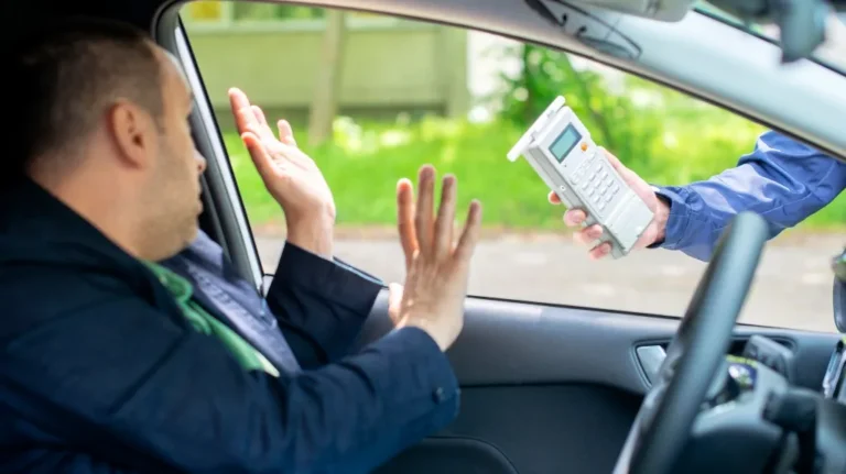 Man inside car raising hands toward a person outside holding a breathalyzer device.