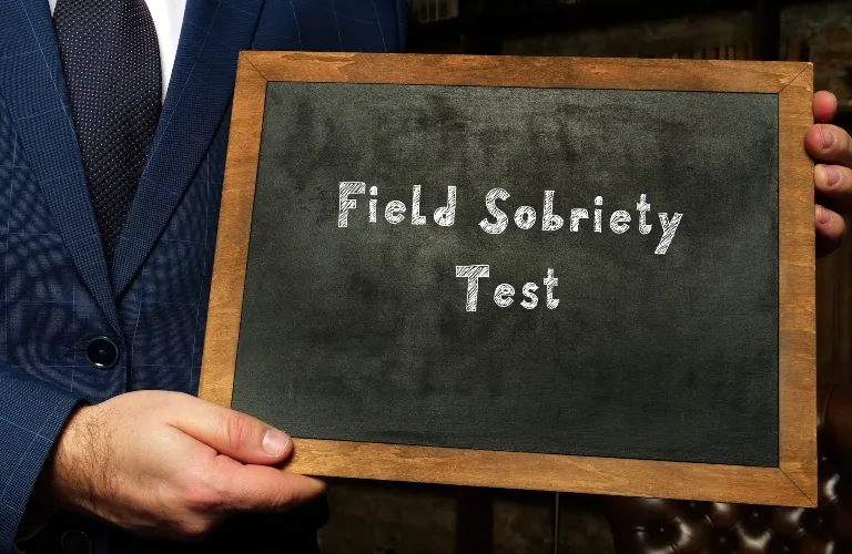 Man in blue suit holding wooden-framed chalkboard with "Field Sobriety Test" text.