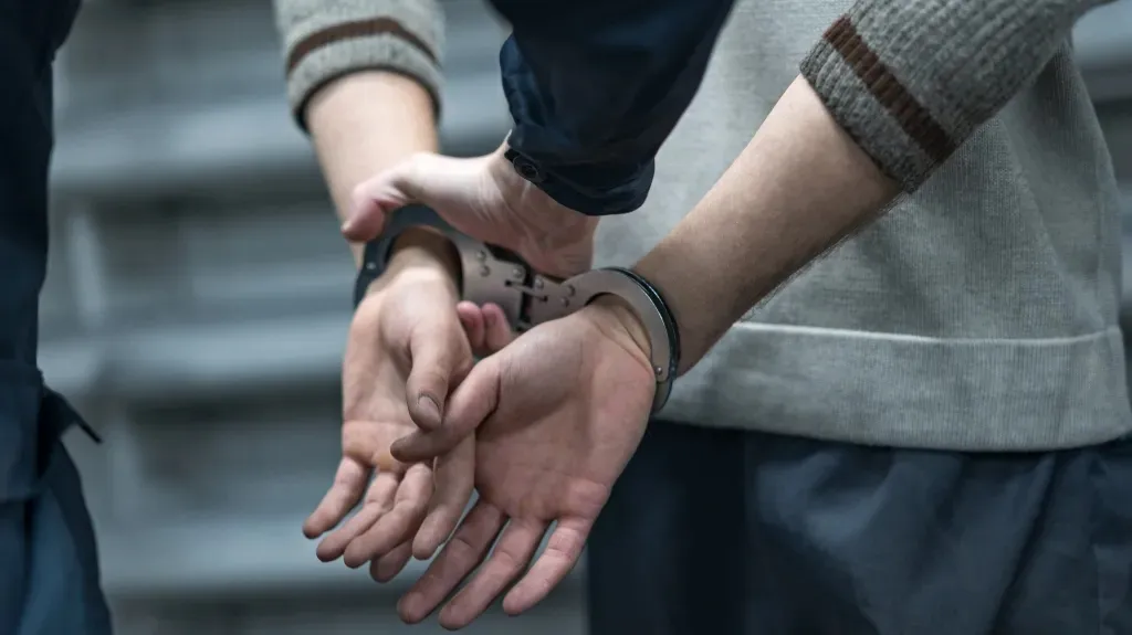 Close-up of a person in handcuffs with another individual holding the cuffs, both wearing long sleeves.